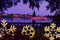 Beautiful scenery with illuminated holidays ornaments, christmas trees over lake, roller coaster and sky tower at sunset backgroun Royalty Free Stock Photo