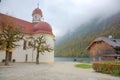 Beautiful scenery of Lake Konigssee with famous Sankt Bartholomae pilgrimage church by the lakeside and autumn mountains in foggy Royalty Free Stock Photo