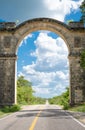 Beautiful scenery of a long, straight, empty road, surrounded by trees, passing through a stone arch Royalty Free Stock Photo