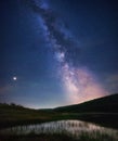 Beautiful scenery of Milky Way galaxy in the night sky over a lake in a grassy field