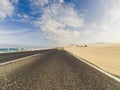Beautiful scenic road with desert sand dunes and beach with blue ocean water on sides - blue sky with clouds in background - Royalty Free Stock Photo