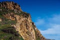 Beautiful scenic view of high rock mountain cliff peak covered with green grass, trees bushes on background of blue sky. Royalty Free Stock Photo