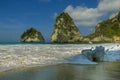 Tropical paradise desert beach with rock cliffs in the horizon under a summer blue sky with sea waves splashing foam in the sand Royalty Free Stock Photo