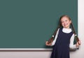 Beautiful school girl with pigtail smiled near blank chalkboard background, dressed in classic black suit, education concept Royalty Free Stock Photo