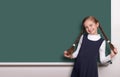 Beautiful school girl with pigtail smiled near blank chalkboard background, dressed in classic black suit, education concept Royalty Free Stock Photo