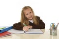 Beautiful schoolgirl in school uniform with blond hair smiling happy sitting on desk doing homework Royalty Free Stock Photo