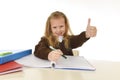 Beautiful schoolgirl in school uniform with blond hair smiling happy sitting on desk doing homework Royalty Free Stock Photo