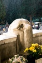 Beautiful sculpture of a girl made of marble/stone sitting and crying above a grave with flowers Royalty Free Stock Photo