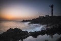 Beautiful sea ocean landscape with big powered waves on the rocks during sunset with classic lighthouse in background -concept of