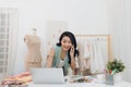 Beautiful seamstress using laptop and phoning while working at her workshop.Dressmaker using laptop