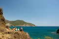 Beautiful seascape. Four women tourists sit on steep bank, relax and enjoy view of turquoise Mediterranean Sea and mountains