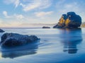 Beautiful seascape. A rock in the middle of the ocean and a lot of stones. Pure clear blue water. Blue sky and light white clouds Royalty Free Stock Photo