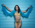 Beautiful seductive brunette woman wearing yellow bikini and blue feather boa looking into the camera and posing over blue