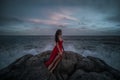 Beautiful seductive woman in red dress enjoying herself on rocks by the sea Royalty Free Stock Photo