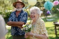 Beautiful senior birthday woman receiving flowers as gift. Garden birthday party for senior lady. Royalty Free Stock Photo