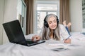 Beautiful senior concentrated businesslady in headphones, writing notes while watching video online webinar, learning or