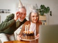 Beautiful senior couple in party hats celebrating birthday at home online on laptop Royalty Free Stock Photo