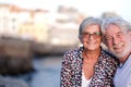 Beautiful senior couple smiling in outdoor at sea at sunset llight looking at camera. Caucasian couple white haired