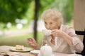 Beautiful senior lady with curly white hair drinking tea in outdoors cafe or restaurant Royalty Free Stock Photo