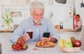 Beautiful senior man white hair having breakfast at home looking social media on smart phone Royalty Free Stock Photo