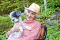 Beautiful Senior smiling woman with straw hat hugging her dog in the mountain