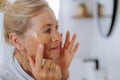 Beautiful senior woman in bathrobe, applying eye patches for puffiness while looking in the mirror Royalty Free Stock Photo