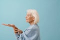 Beautiful senior woman in blue pullover holding empty opened hand