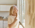 Beautiful senior woman with hairbrush looking in window while enjoying new day at home Royalty Free Stock Photo