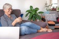 Beautiful senior woman relaxing on sofa at home using mobile phone. Smiling elderly lady enjoying tech and social Royalty Free Stock Photo