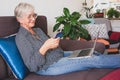 Beautiful senior woman relaxing on sofa at home using mobile phone. Smiling elderly lady enjoying tech and social Royalty Free Stock Photo