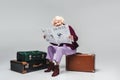 beautiful senior woman sitting on vintage suitcase and reading travel newspaper