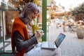 Beautiful senior woman uses videochat on laptop sitting on bench near cafe