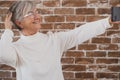 Beautiful senior woman using phone standing against a brick wall smiling Royalty Free Stock Photo