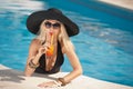 Beautiful sensual blonde with fashionable sunglasses relaxing in the pool with a juice. Attractive long hair woman in black Royalty Free Stock Photo