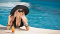 Beautiful sensual blonde with fashionable sunglasses relaxing in the pool with a juice. Attractive long hair woman in black Royalty Free Stock Photo