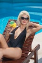 Beautiful sensual blonde with fashionable sunglasses relaxing at swimming pool with a juice. Attractive long fair hair woman Royalty Free Stock Photo
