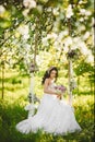 Beautiful and sensual brunette model girl in white lace dress with bouquet of flowers in her hands sits on a hanging swings decora Royalty Free Stock Photo