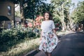 Beautiful sensual brunette young woman in white blouse and skirt with flowers close to red roses. She stands near the rose bush. Royalty Free Stock Photo