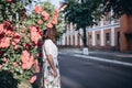 Beautiful sensual brunette young woman in white blouse and skirt with flowers close to red roses. She stands near the rose bush Royalty Free Stock Photo