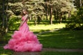 Sensual woman in pink evening dress with fluffy skirt is posing in botanical garden on the grass surrounded by the woods Royalty Free Stock Photo