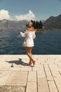 Beautiful sensual woman with blond hair in elegant dress and straw hat and bag, posing in Montenego`s city Perast Royalty Free Stock Photo