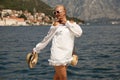 Beautiful sensual woman with blond hair in elegant dress and straw hat and bag, posing in Montenego`s city Perast Royalty Free Stock Photo