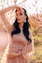 Beautiful sensual woman with dark hair in elegant dress posing among flowering peach trees Royalty Free Stock Photo