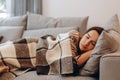 Beautiful serene woman sleeping on comfy sofa under warm cozy plaid in modern living room. Healthy daytime nap, tiredness relief,