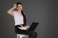 Beautiful serious brunette girl in white t-shirts sits on chair with book and using laptop Royalty Free Stock Photo