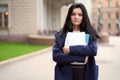 Beautiful serious smart girl brunette student holding notebooks and textbooks, stands at University on street of St. Petersburg. A