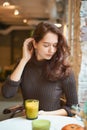Beautiful serious stylish fashionable smart girl is sitting in cafe and drinking healthy yellow smoothie or latte vegan. Charming