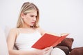 Beautiful serious young woman reading a book, relaxing at home