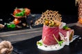 Beautiful serving of slice salted tuna with vegetables in a creamy sauce on a dark plate on a rustic wooden tray