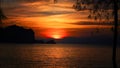 A beautiful setting sun behind the silhouette of hills and tree branches with its reflection over the sea waves at Tanjung Rhu Royalty Free Stock Photo